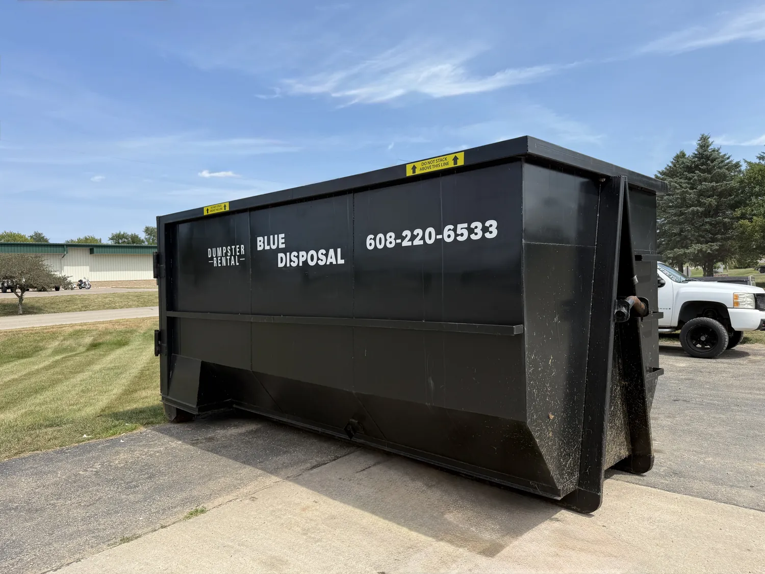 Dumpster parked on a paved driveway under a clear sky